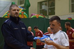 Policjant przekazuje nagrodę dla zwycięskiej drużyny w turnieju piłki nożnej na hali OSIR w Tucholi.